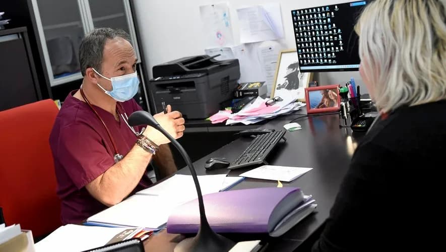 Médecin masqué en blouse, en consultation à son bureau de cabinet